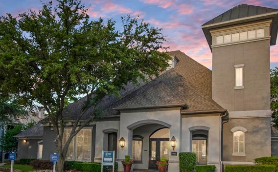 A charming residential building surrounded by lush trees, set against a colorful sunset sky.