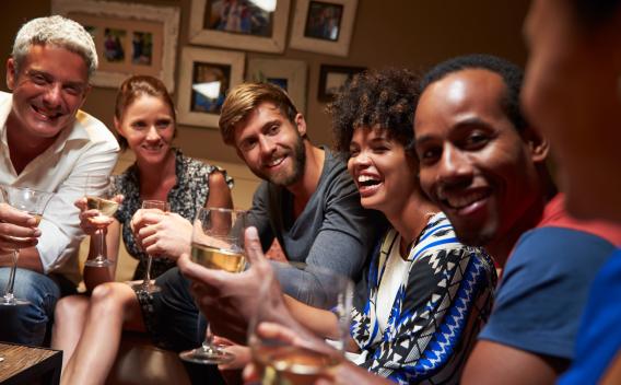 A group of friends enjoys drinks and laughter together in a warmly lit living room.