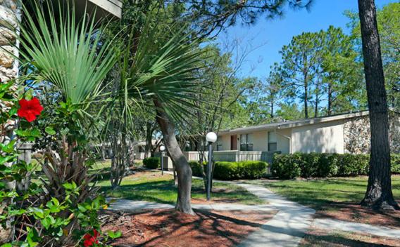 Image 2: An exterior view of an apartment building with a sidewalk and flowerbed in the foreground, surrounded by trees and greenery.