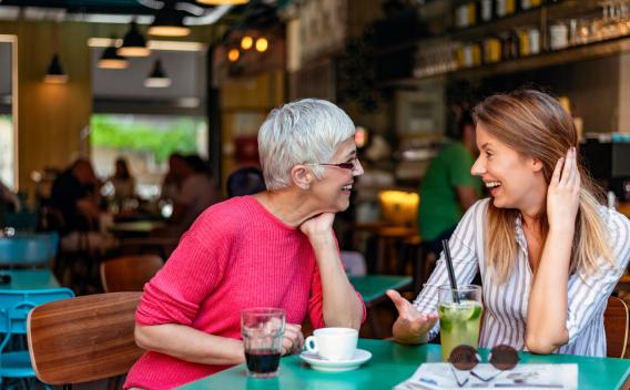 Two women, one older and one younger, smiling and engaged in a lively conversation at a café.