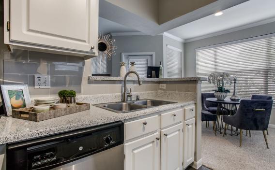 Modern kitchen with granite countertops, stainless steel appliances, and an open concept design leading into a brightly lit living room with large windows at Arboretum Estates.