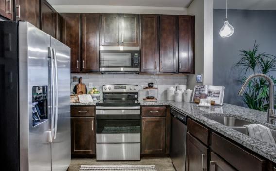 A modern kitchen with dark wood cabinetry, stainless steel appliances, and a granite countertop with a double sink.