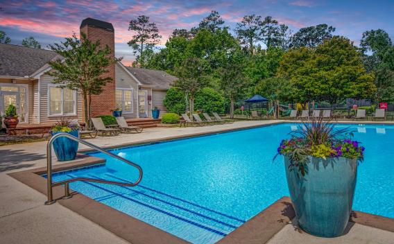Resort-style swimming pool at Amber Chase Apartments with lounge chairs and landscaped surroundings at sunset.