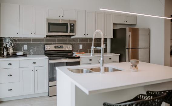 A modern kitchen in Industry Columbus Apartments featuring sleek white cabinetry, stainless steel appliances, and a stylish island with a dual sink and high-arc faucet.