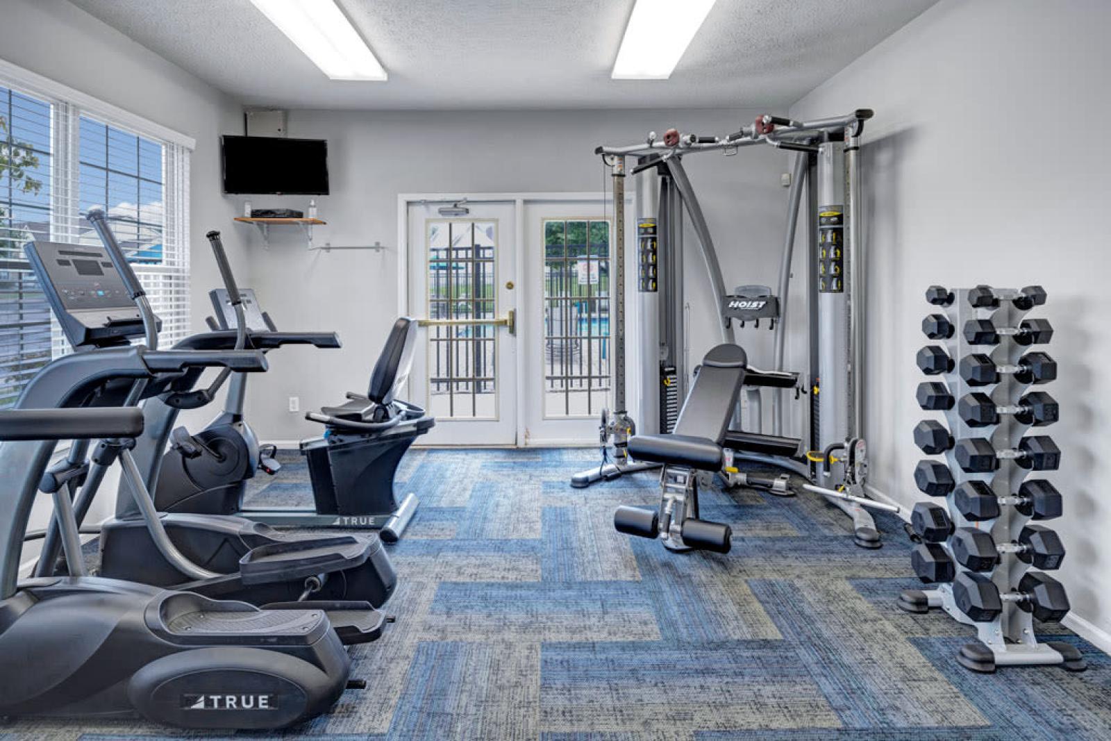 A fully equipped fitness center with modern cardio machines, weight training equipment, and ample natural light.