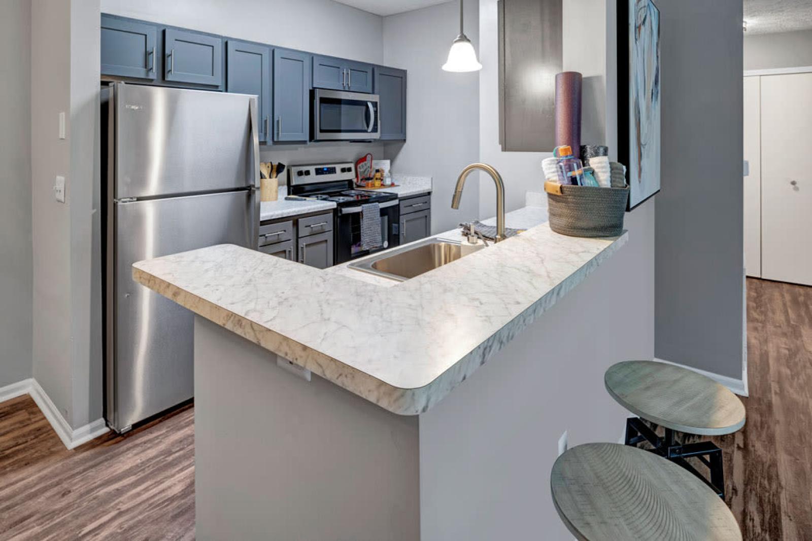 Modern kitchen at Trotter's Landing Apartments with stainless steel appliances, marble-patterned countertops, and sleek gray cabinetry.