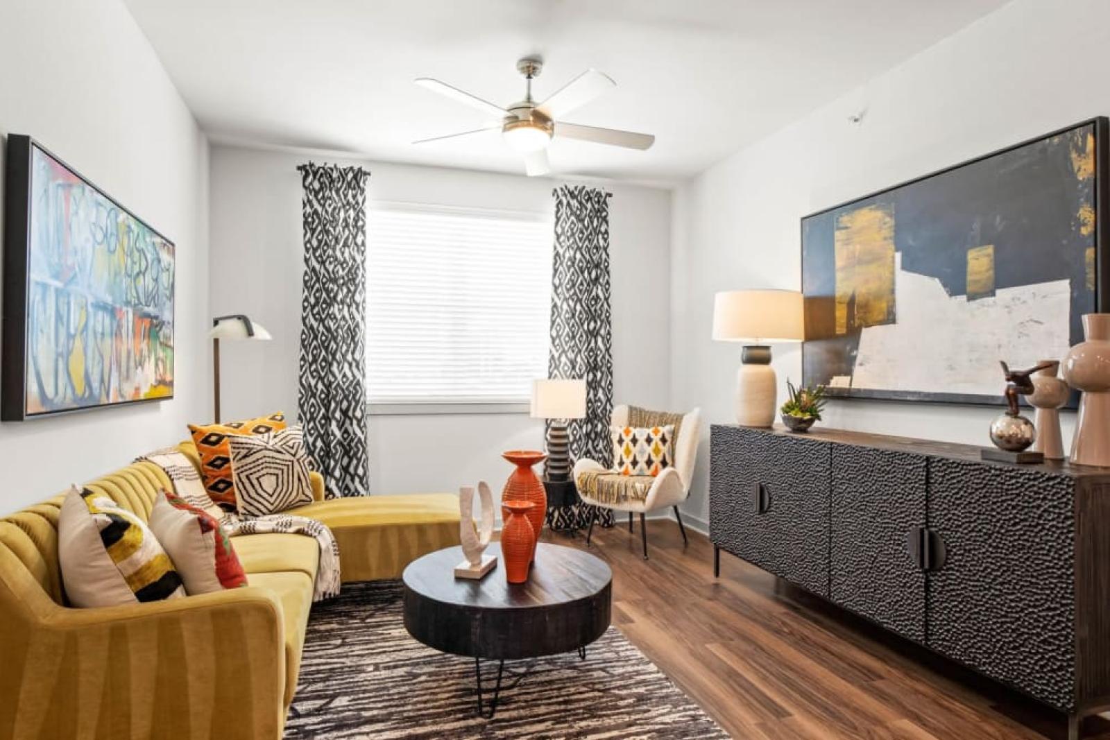 A modern living room featuring a yellow sectional sofa, patterned curtains, and abstract artwork on the walls.