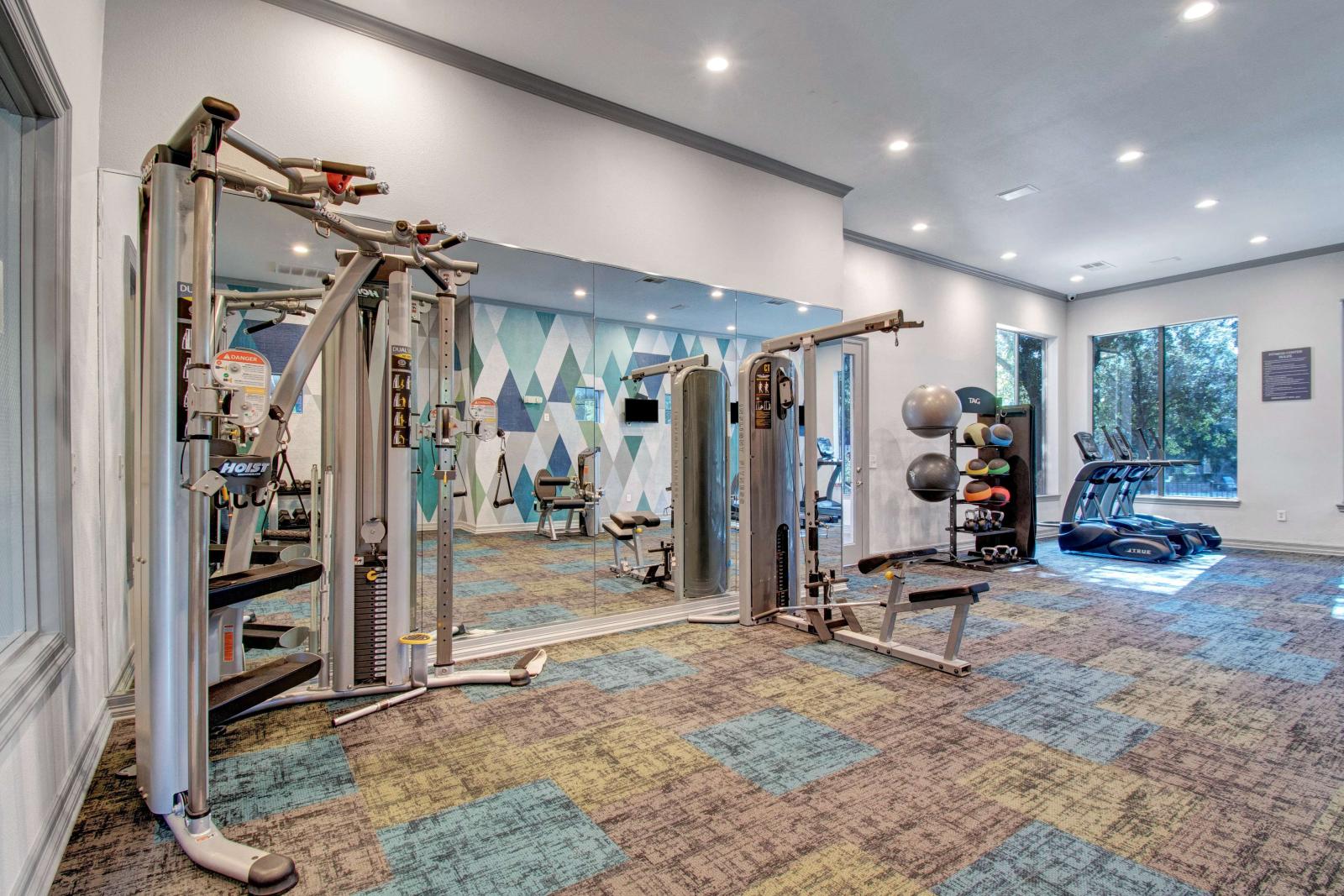Spacious fitness center with modern workout equipment, colorful carpet tiles, and large mirrors.