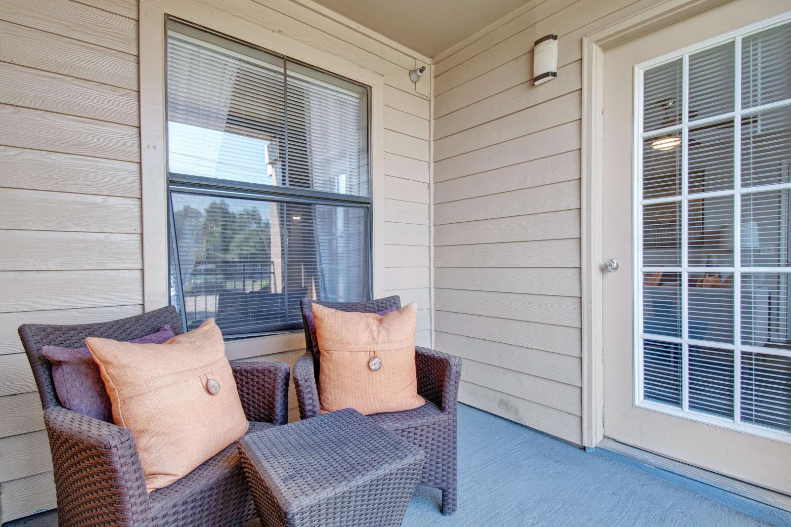 Private balcony with wicker chairs and a small table, adjacent to a large window and French door.