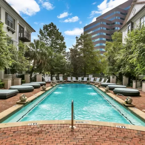 Rectangular pool with cushioned loungers, vibrant landscaping, and modern apartments in the background.