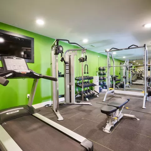 Fully equipped fitness center featuring treadmills, strength training machines, and a mirrored wall with a bright green accent wall.
