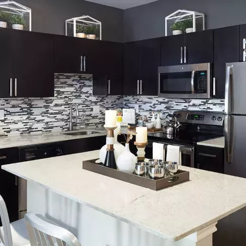 Modern kitchen with dark cabinets, stainless steel appliances, and a decorative backsplash, featuring a white island with stools.
