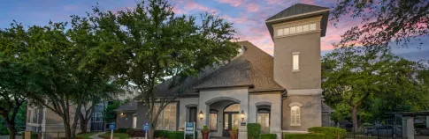 A charming residential building surrounded by lush trees, set against a colorful sunset sky.