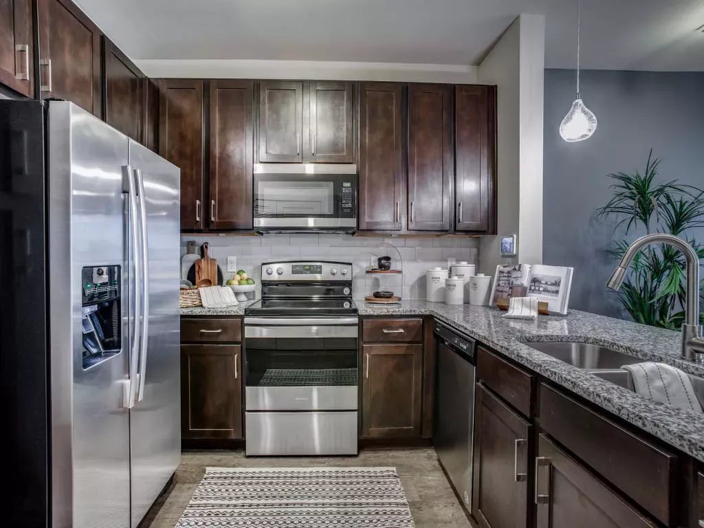A modern kitchen with dark wood cabinetry, stainless steel appliances, and a granite countertop with a double sink.