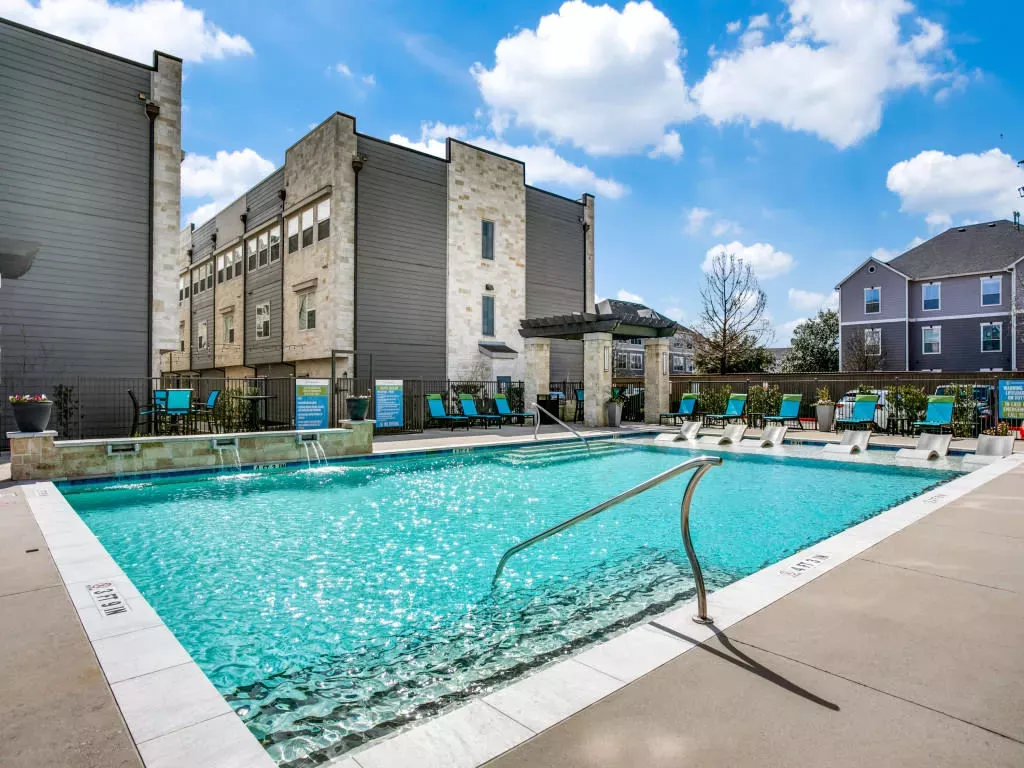 A sparkling blue swimming pool surrounded by lounge chairs, with contemporary apartment buildings in the background.