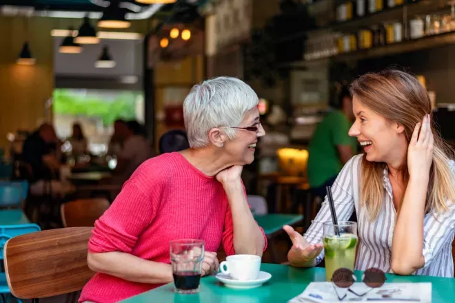 Two women, one older and one younger, smiling and engaged in a lively conversation at a café.