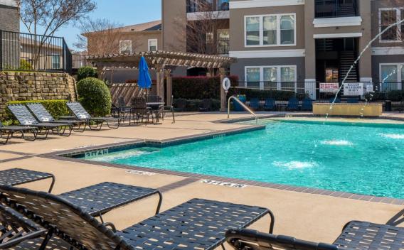 Outdoor swimming pool area with lounge chairs, fountains, and a shaded seating space.