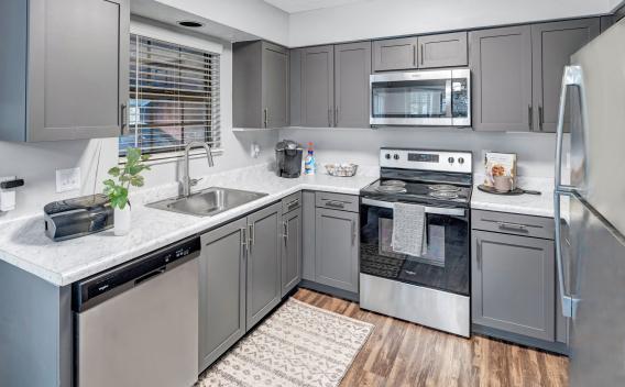 A contemporary kitchen with gray cabinets, marble countertops, stainless steel appliances, and a window above the sink letting in natural light.