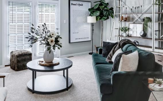 A modern living room with a dark green velvet sofa, cozy fireplace, stylish shelving, and large windows creating a bright and inviting space.