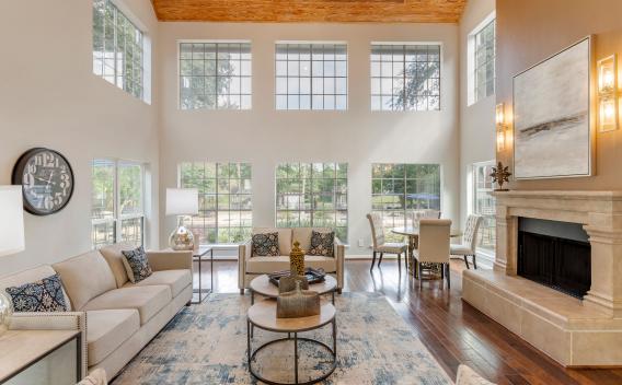 A bright, spacious living room with tall windows, elegant beige sofas, a fireplace, and modern decor accents.