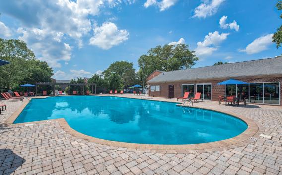 Resort-style swimming pool at Maple Bay Apartments, complete with lounge chairs, umbrellas, and a clubhouse in the background.