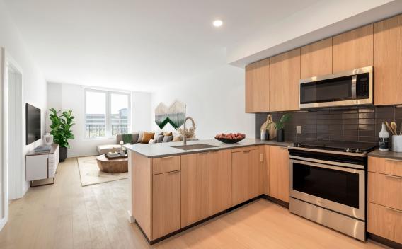 Modern kitchen featuring stainless steel appliances, wood cabinetry, and a sleek tile backsplash at The Edmund Apartments.