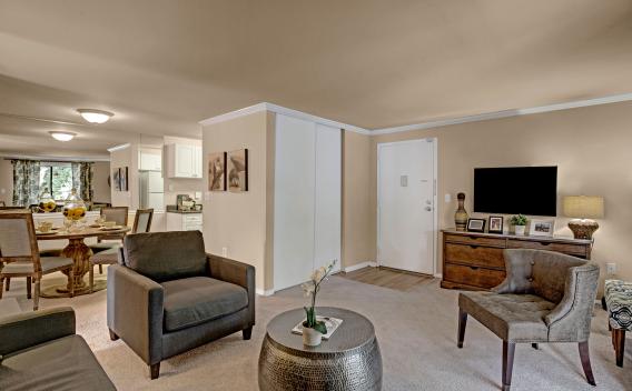 A spacious and elegantly furnished living room at The Hamptons at Town Center in Germantown, MD, featuring a cozy seating area, stylish decor, and a view of the adjacent dining space and kitchen.