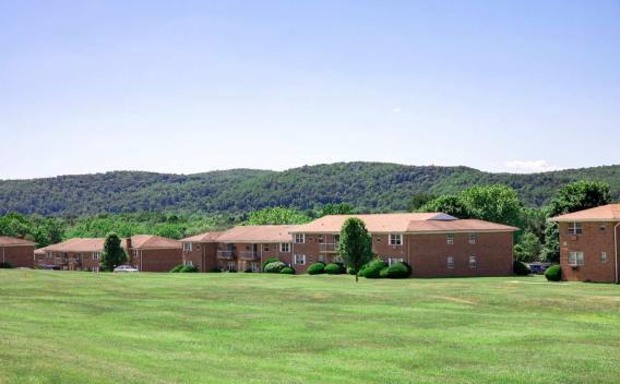 A scenic view of Washington Gardens Apartments in Washington, NJ, surrounded by lush green lawns and picturesque wooded hills in the background. Ideal for highlighting the serene and spacious environment of the community.