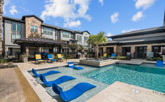 A luxurious outdoor pool area with blue lounge chairs, a shaded cabana, and resort-style landscaping.