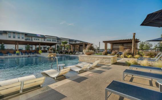 A serene outdoor pool with sun loungers and shaded pergolas, surrounded by landscaping.