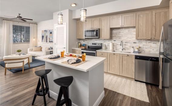 A stylish open-concept kitchen featuring sleek cabinetry, stainless steel appliances, and a spacious island, seamlessly flowing into a cozy living area with natural light.