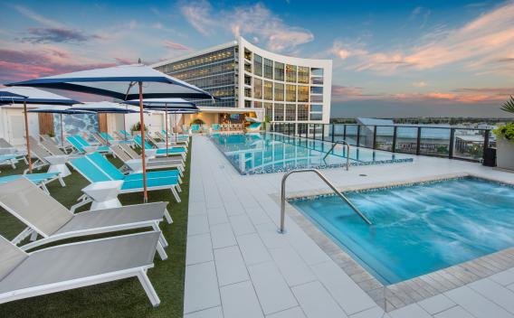 Rooftop pool at The Flats at City Place Luxury Apartments with modern lounge chairs, shaded cabanas, and stunning sunset views over the city skyline.