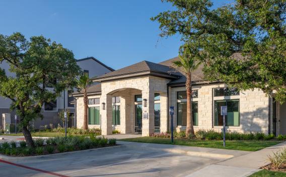 The leasing office exterior features a modern design with a stone facade, arched entryway, and lush landscaping, creating an inviting welcome to Vista At Town Green Luxury Apartments.