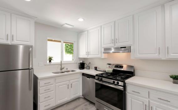 Contemporary kitchen with white cabinetry, stainless steel appliances, and a double sink beneath a window.