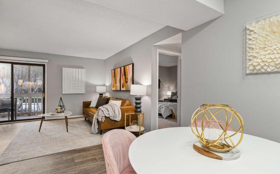 Modern apartment interior with a cozy leather sofa, abstract wall art, and a view of the bedroom and outdoor patio through sliding glass doors, accented by soft lighting and stylish decor.