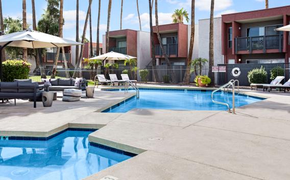 Pool area with lounge chairs, shaded seating, and palm trees at a modern apartment community.