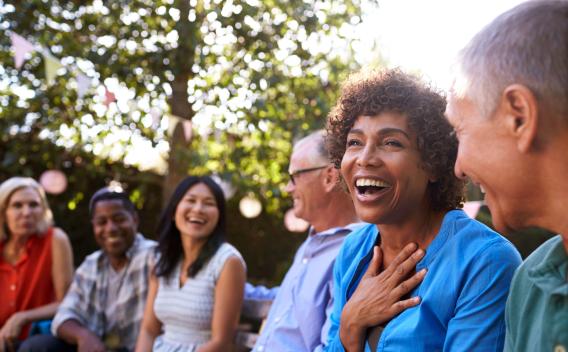 Group of seniors laughing and socializing at an outdoor gathering, seated in a garden with string lights and festive decorations.