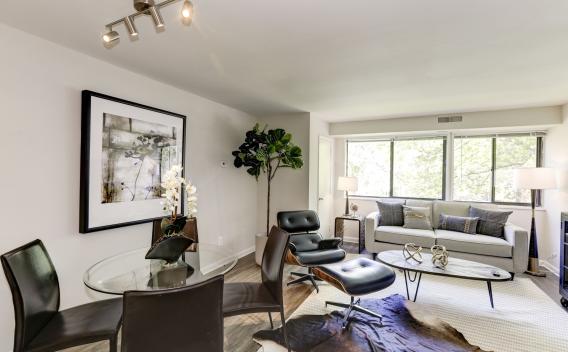  A stylish and modern living and dining area at The Landings II Apartments, featuring a contemporary glass dining table, sleek black chairs, and a cozy seating area with a large window providing natural light.