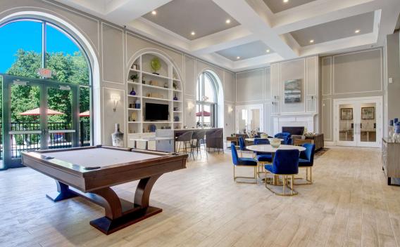 Spacious resident lounge featuring pool table, tall arched windows, and built-in shelving with decor.