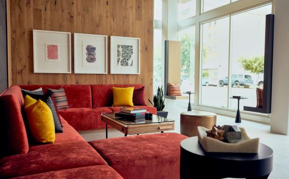Contemporary resident lounge featuring a red sectional sofa, large windows, wood accent wall, and colorful artwork.