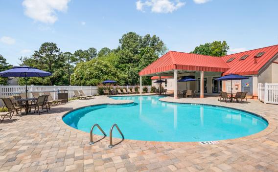 Outdoor swimming pool at The Samuel with lounge chairs, shaded tables, and a red-roofed pavilion surrounded by lush greenery