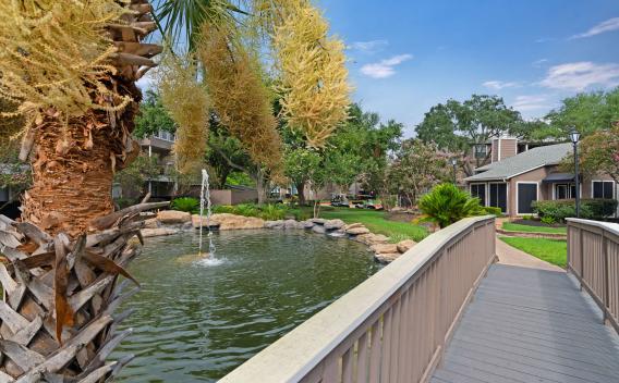 Serene pond with fountain, surrounded by palm trees, landscaping, and residential buildings.