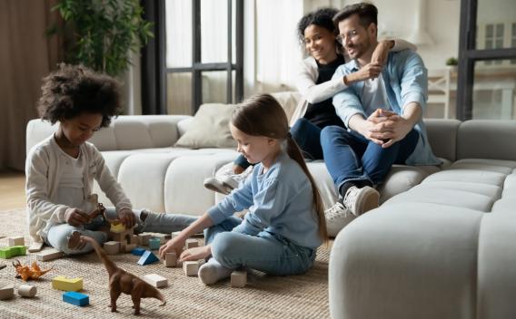Parents on a couch with children playing with toys on the floor in a living room