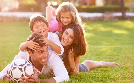 Family of four outside in a pile on the grass with the dad holding a soccer ball a 