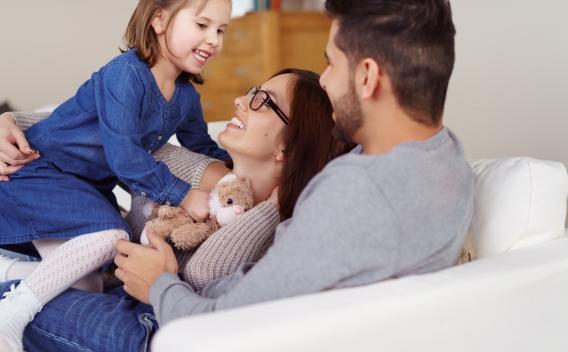 Mother and father on a couch playing with daughter who has a stuffed animal in her hand
