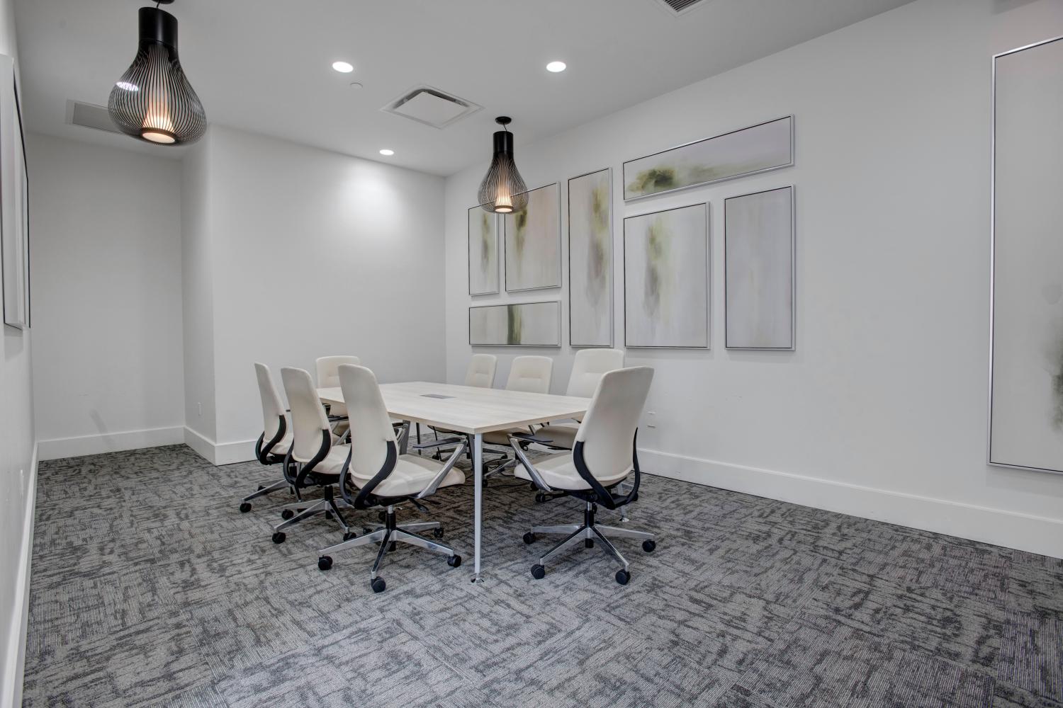 Professional meeting room with a large conference table, white chairs, and modern pendant lighting.