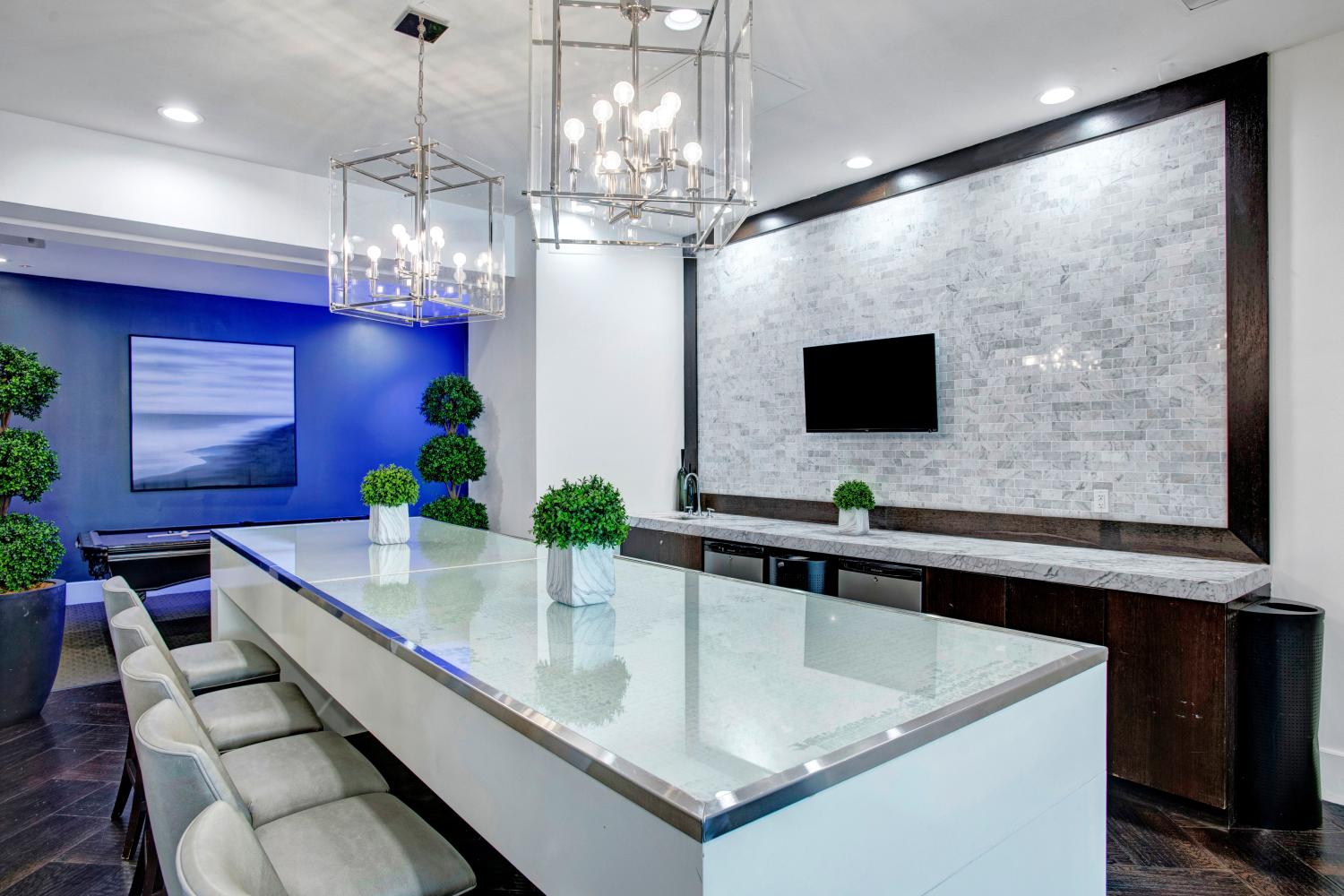 Elegant community kitchen featuring a large glass-top island, modern lighting fixtures, and a sleek design with marble accents.