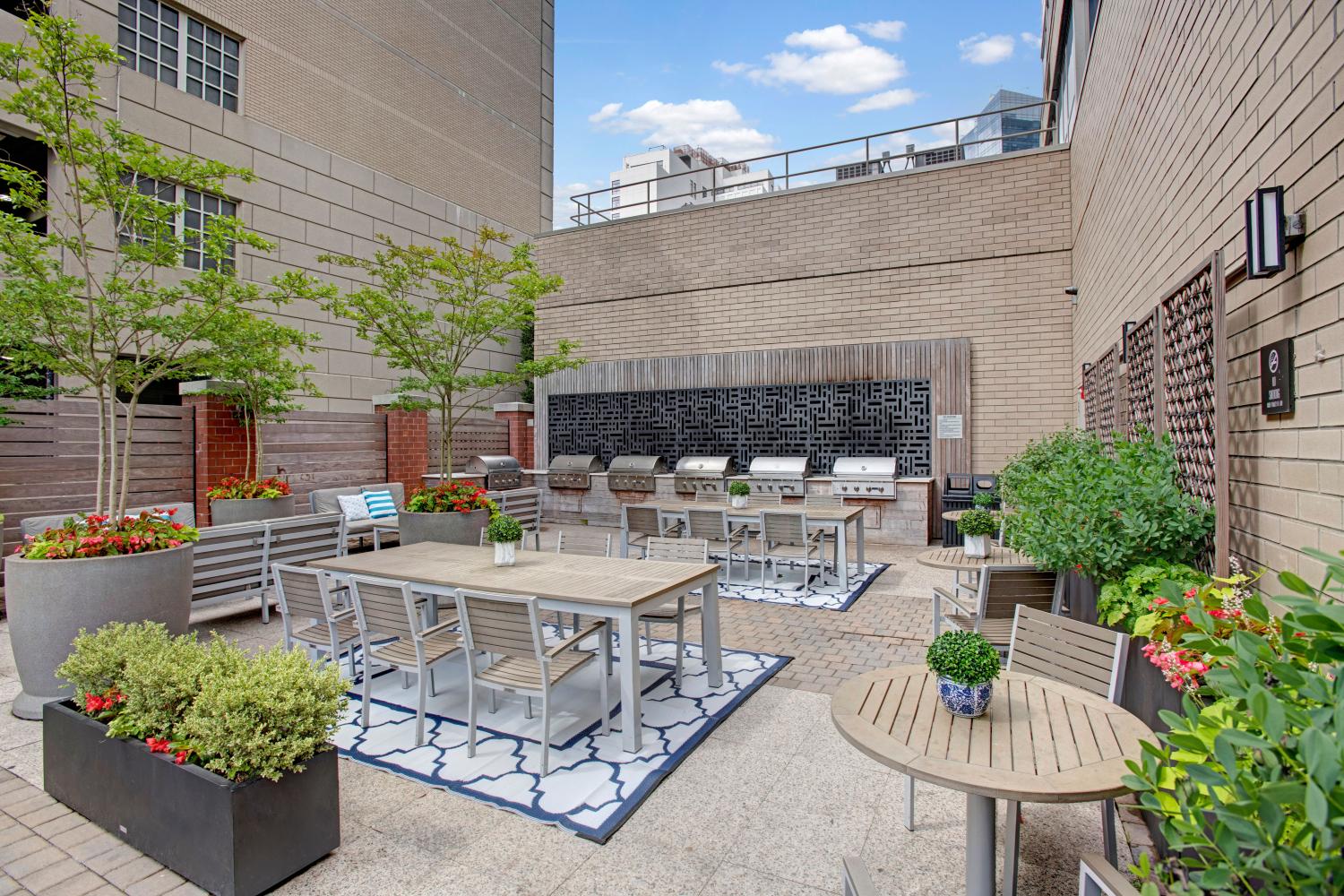 An outdoor grilling and dining space with stainless steel grills, tables, and vibrant greenery for social gatherings.
