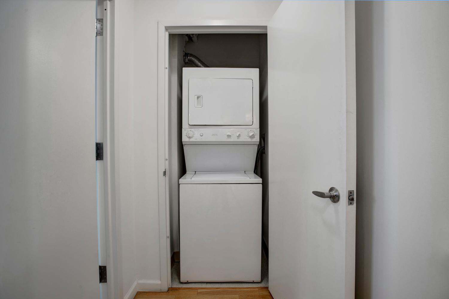 A compact laundry area featuring a stacked washer and dryer unit tucked behind white closet doors, offering convenient in-home laundry access at Skyline New Rochelle Luxury Apartments.