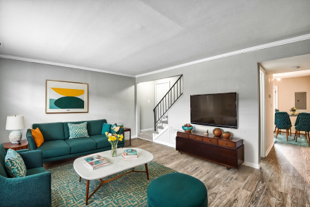 Fully staged living area at Maple Bay Apartments, featuring modern furniture, a mounted TV, and access to the dining area.